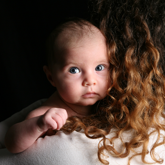 fotograf babyfotos und kinderfotos. kleines baby blickt über die schulter seiner mutter in die kamera