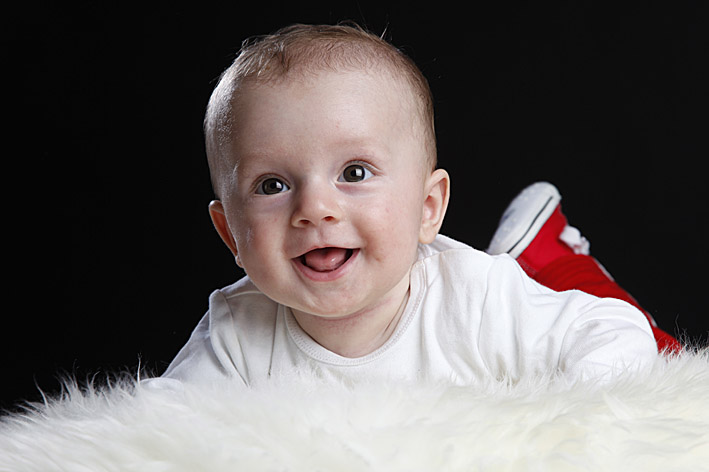 lachendes baby mit roten turnschuhen auf schaffell im fotostudio münchen