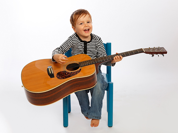 der fotograf münchen machte dieses kinderfoto, ein junge mit gitarre lacht in die kamera