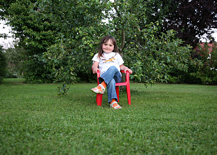 kinderfoto münchen in farbe, lea auf rotem stuhl vor apfelbäumchen